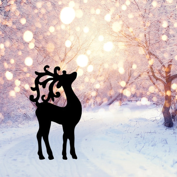Silhouette of an elegant reindeer precut in black Oceanside coe 96 glass, placed against a snowy forest background with tall pine trees and mountain peaks at sunrise.